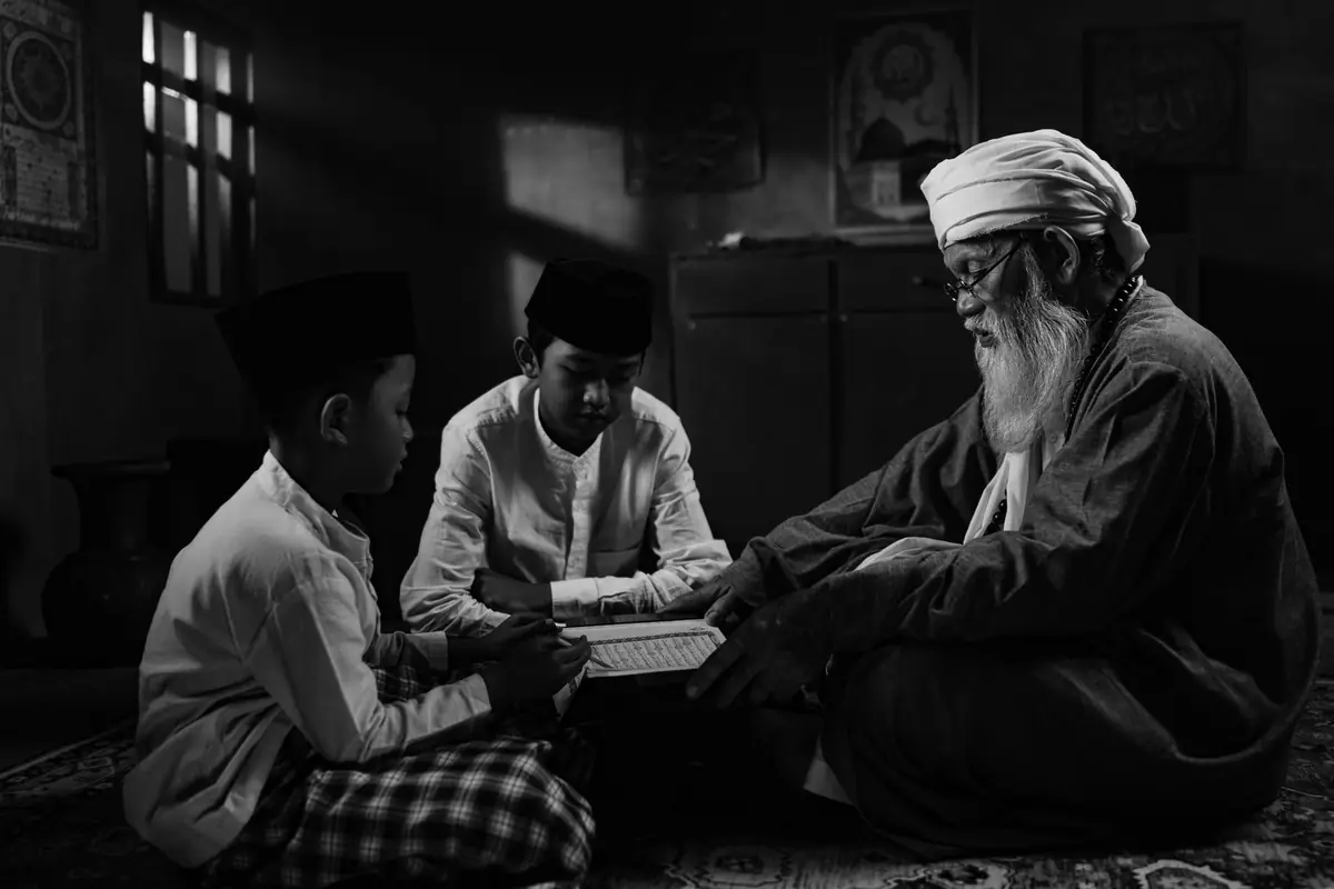 Seorang sesepuh mengajar dua anak membaca kitab, foto hitam putih