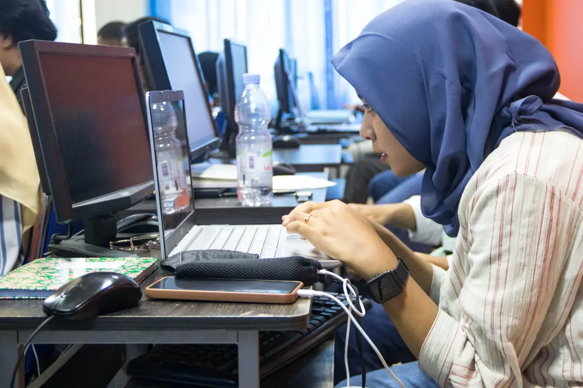Perempuan berkerudung mengetik di laboratorium komputer
