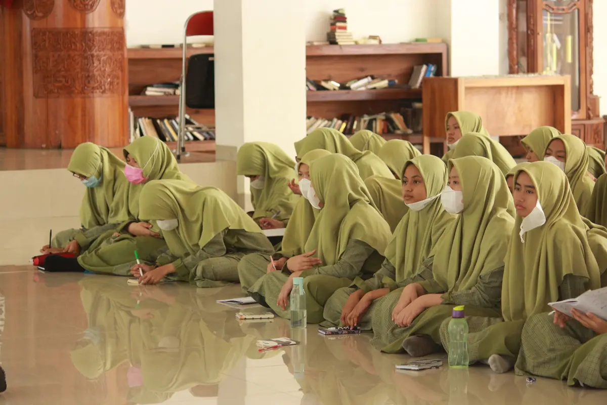 Santriwati berkerudung hijau belajar bersama di aula dengan rak buku di belakangnya